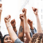 Group of young people marching together in the city downtown protesting .
