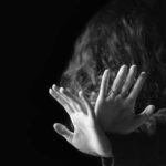 Concept of a violence against women. Black and white portrait of scared and desperate woman, focus on the hands in protective gesture