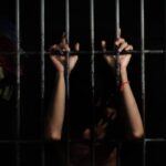 hands of a prisoner behind prison bars