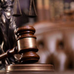 Judge’s gavel, Themis sculpture and collection of legal books on the brown background.