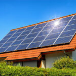 Solar panel on a red roof reflecting the sun and the cloudless blue sky