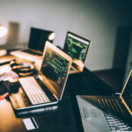 Computer hacker sitting in front of laptop late at night and using phone