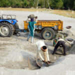 manual-worker-loading-sand-on-tractor-at-river-bank-W197WG