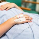 Close-up of a patient's hand with an IV drip in a hospital setting. The hand rests on a blue hospital gown, indicating a medical environment and care. Hospital, medical, and healthcare concept.